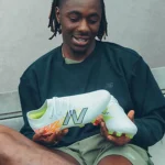 A person holding the New Balance Furon Elite FG V8 soccer cleats, showcasing the lightweight design and textured upper.