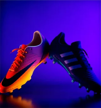 A pair of Nike and Adidas soccer cleats facing off in a competitive lighting setup.